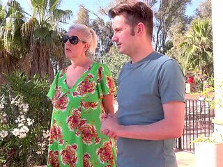 A mature woman with glasses, Maggie Moon, has fun with a young man outdoors.